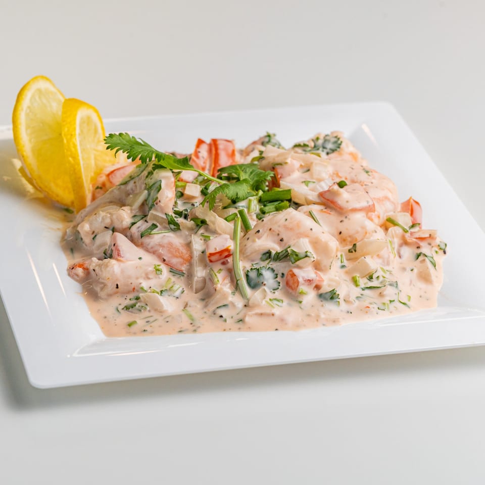 Creamy seafood ceviche with shrimp, red peppers, and cilantro, garnished with lemon wedges.