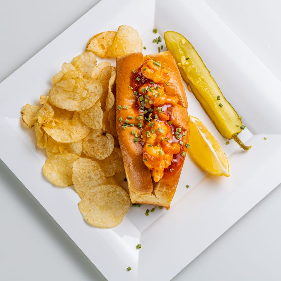 The Hungry Captain's shrimp roll with chips, a pickle spear, and lemon wedge on a white plate.