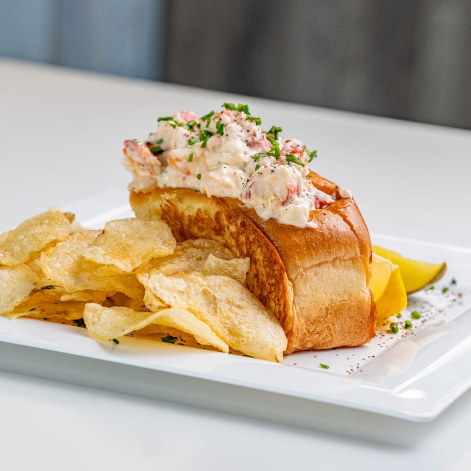 The Hungry Captain's lobster roll with chips and lemon wedges on a white plate.