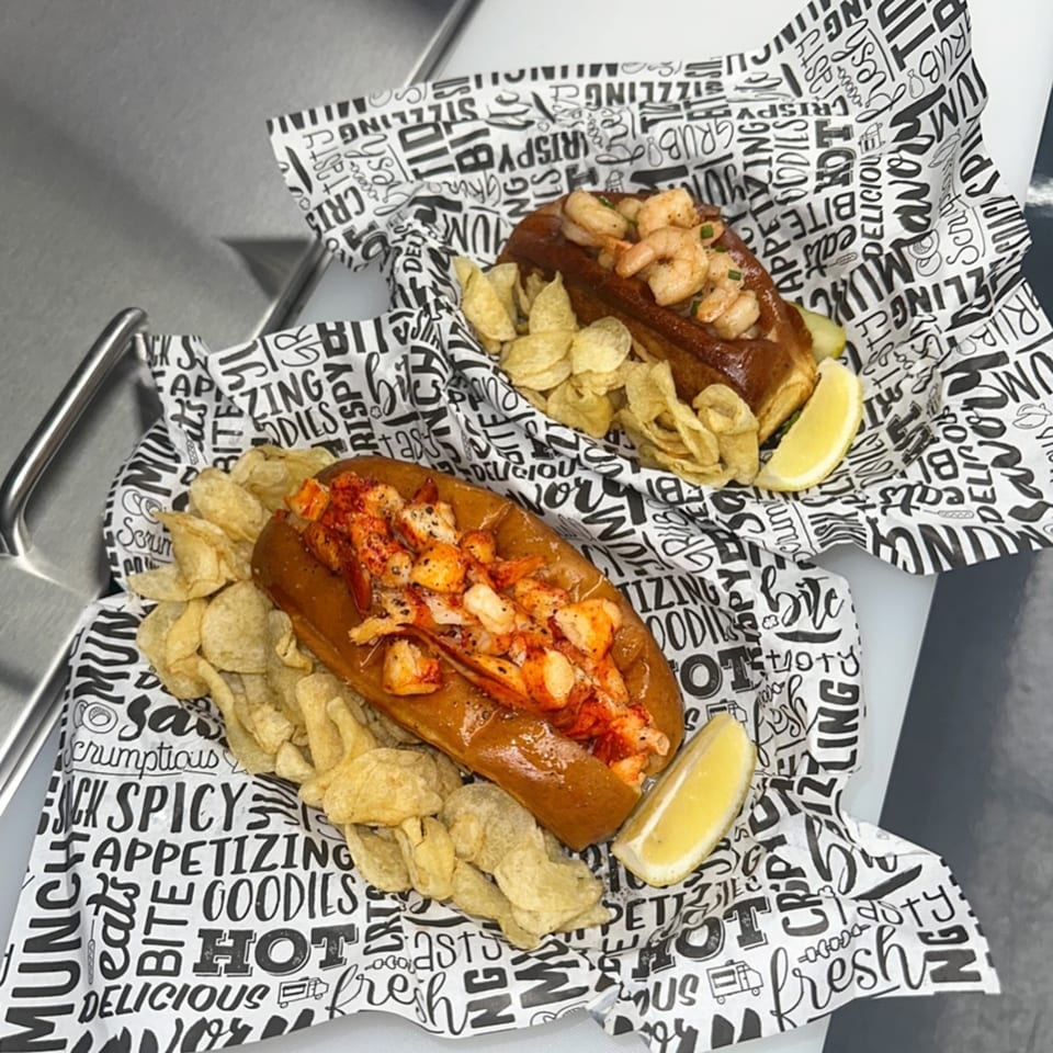 Two Hungry Captain lobster rolls, one with shrimp, served with chips and lemon wedges.