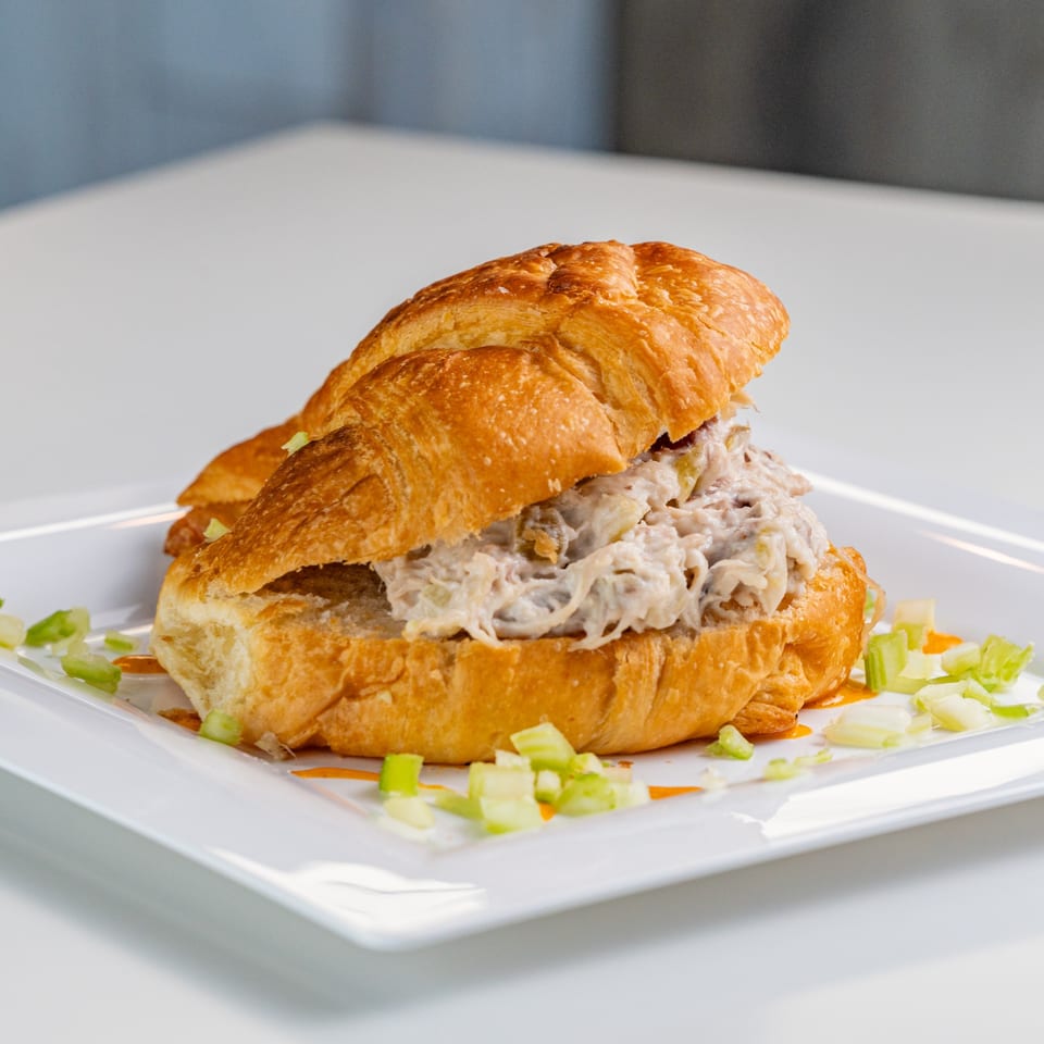 A crab salad croissant sandwich on a white plate, garnished with chopped celery.