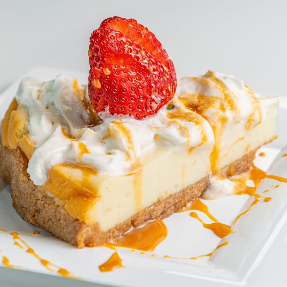 Two slices of cheesecake with whipped cream, caramel drizzle, and a fresh strawberry on a white plate.