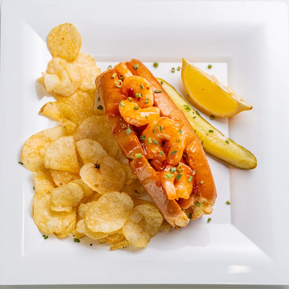 The Hungry Captain's shrimp roll with chips, a pickle spear, and lemon wedge on a white plate.