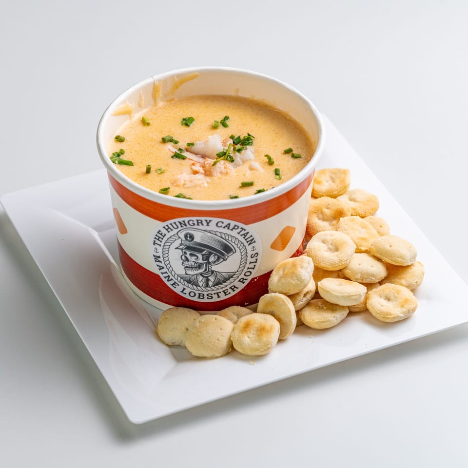 The Hungry Captain's lobster bisque in a branded cup with crackers on a white plate.